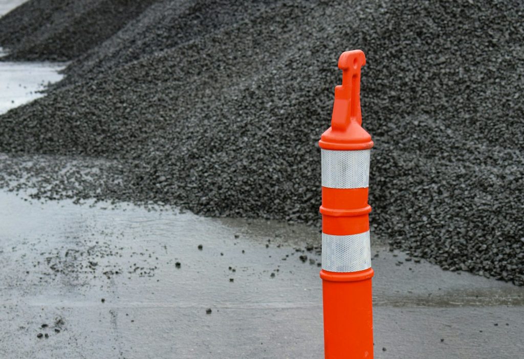 un cône de signalisation orange et blanc à côté d'un tas de graviers
