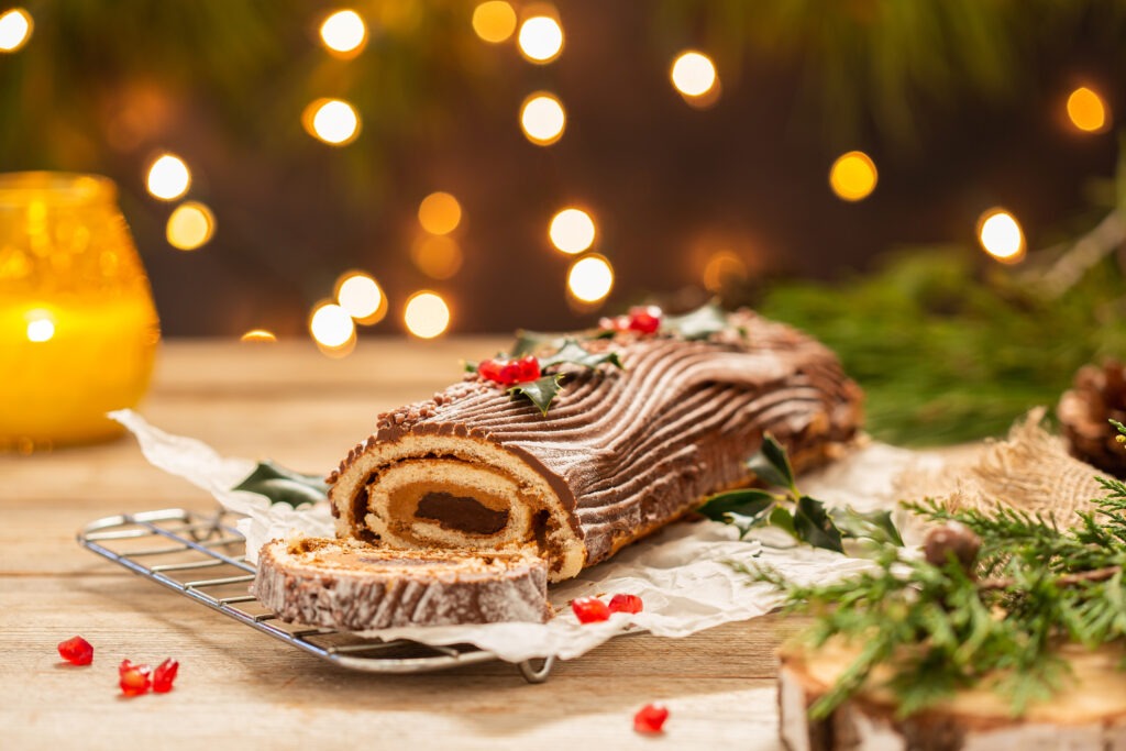 Gâteau de Noël traditionnel, bûche de Yule en chocolat sur une table rustique avec des décorations de fête et des lumières. 
