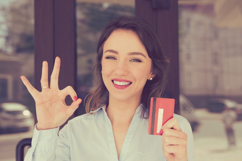 Femme au sourire carnassier tenant une carte de crédit près d'un bureau, d'un magasin ou d'un centre commercial, en extérieur. Concept de shopaholic payant avec une carte de crédit